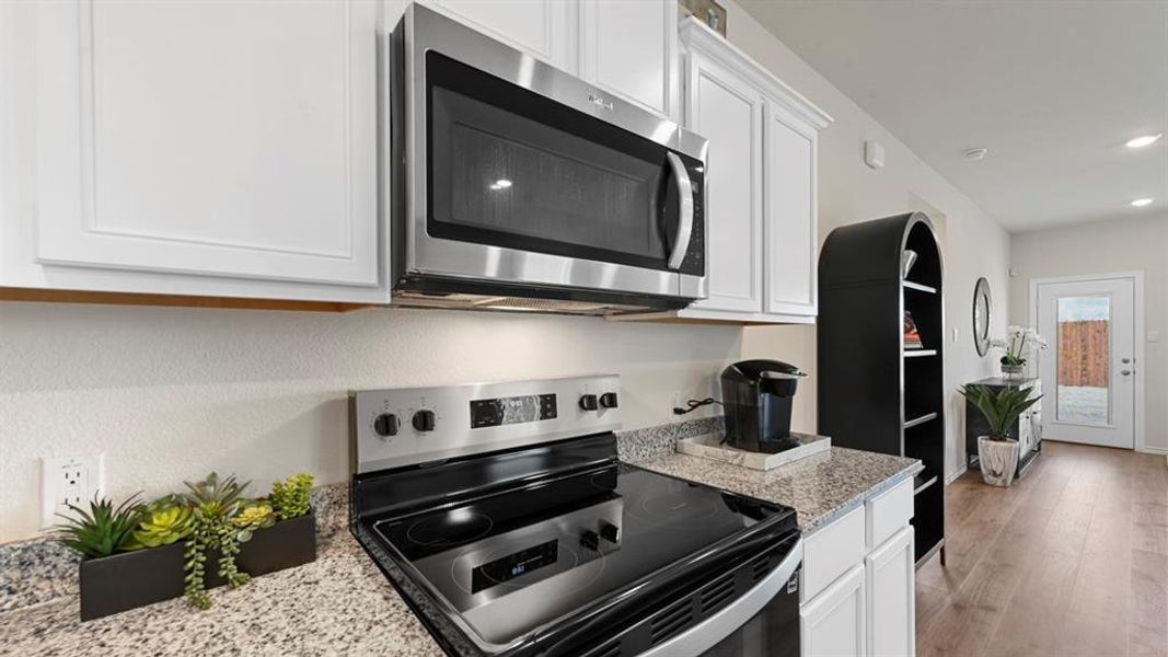 Kitchen with appliances with stainless steel finishes, white cabinets, light stone counters, light wood-style floors, and recessed lighting Kitchen with appliances with stainless steel finishes, white cabinets, light stone counters, light wood-style floors, and recessed lighting