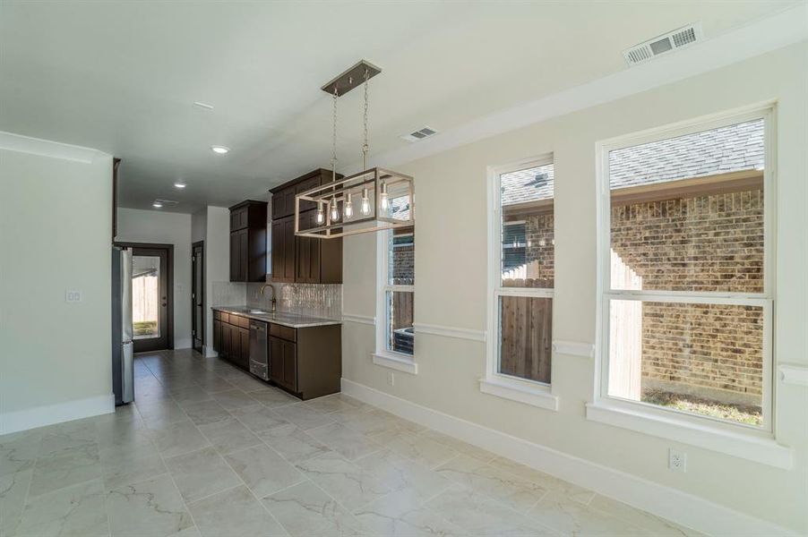 Kitchen with decorative light fixtures, tasteful backsplash, a chandelier, dark brown cabinets, and appliances with stainless steel finishes Kitchen with decorative light fixtures, tasteful backsplash, a chandelier, dark brown cabinets, and appliances with stainless steel finishes
