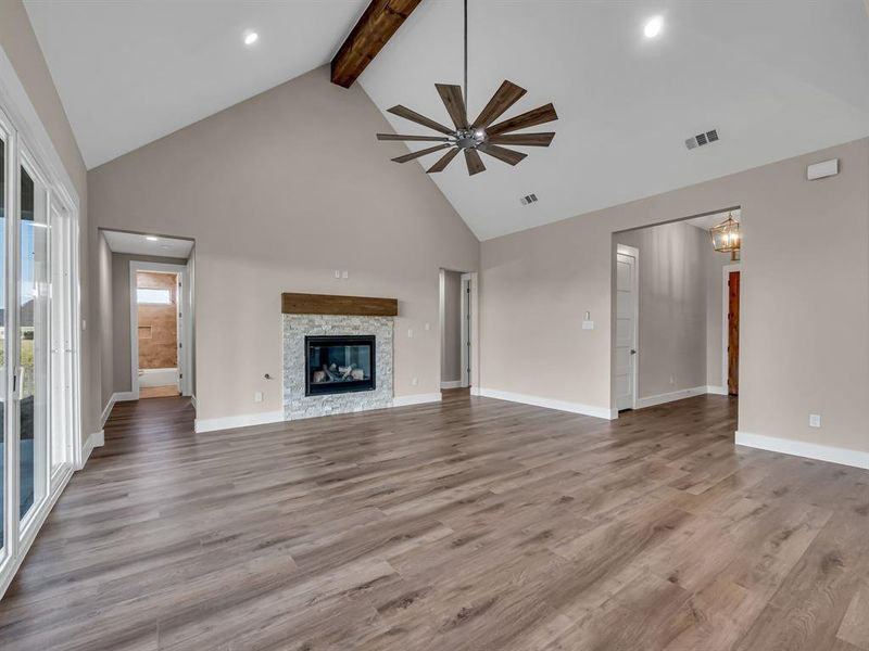 Unfurnished living room featuring beam ceiling, ceiling fan, high vaulted ceiling, light wood-type flooring, and a stone fireplace