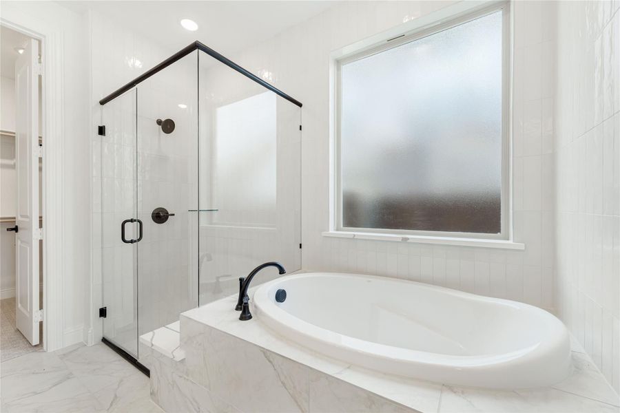 White master bathroom with marble soaking tub, glass-enclosed shower, and frosted window