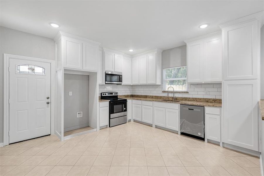 Kitchen with sink, stainless steel appliances, light stone counters, backsplash, and white cabinets