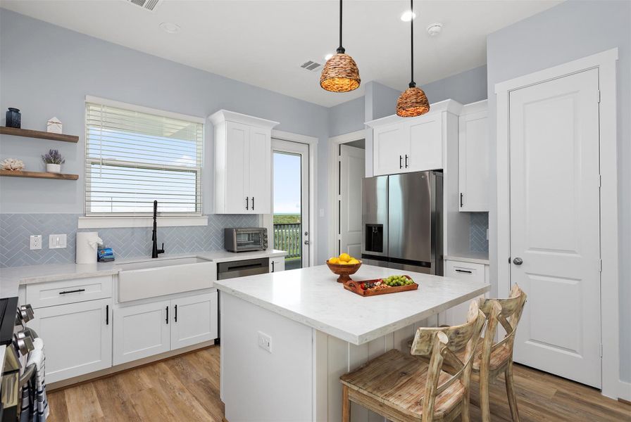 An open kitchen design ensures the cook never misses a moment. Pendant lights illuminate the island, while ample cabinetry and counter space make this kitchen as practical as it is beautiful.