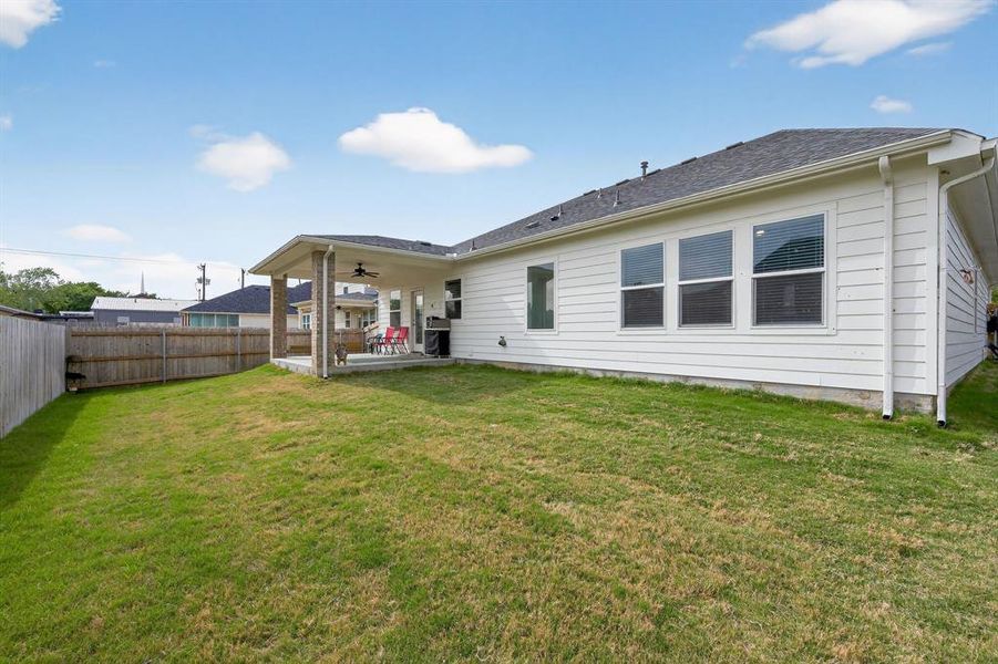 The property features a spacious backyard with a lawn, a covered patio, and a privacy fence