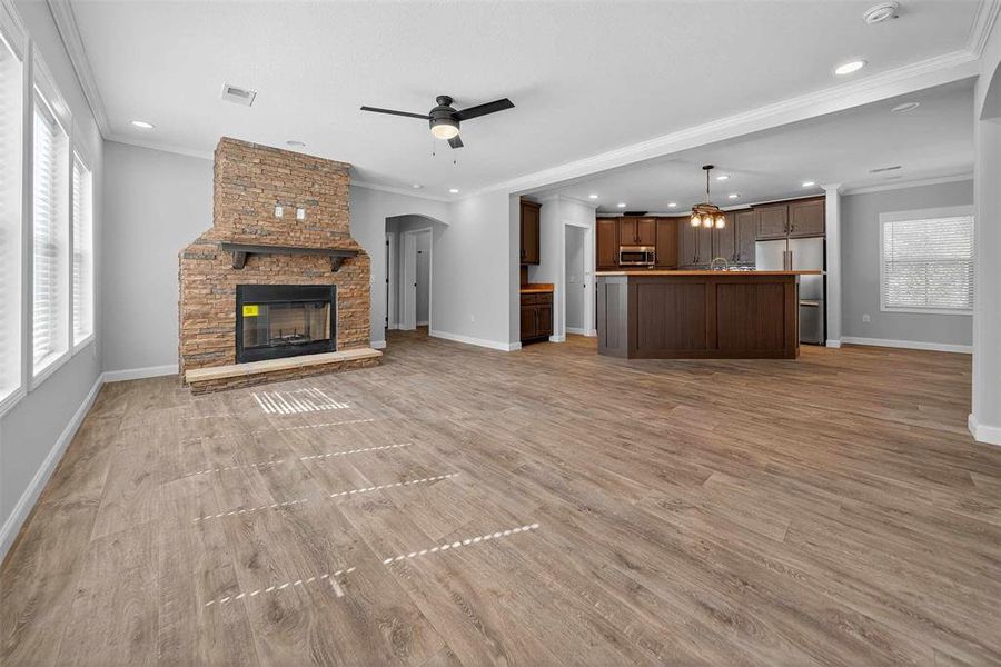 Unfurnished living room featuring plenty of natural light, a fireplace, crown molding, ceiling fan, and arched walkways Unfurnished living room featuring plenty of natural light, a fireplace, crown molding, ceiling fan, and arched walkways