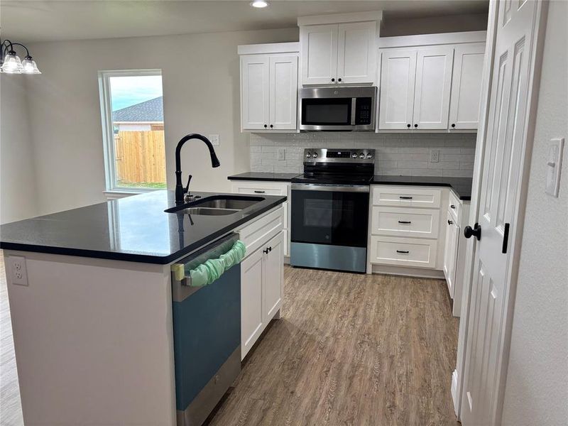 Kitchen with stainless steel appliances, a kitchen island with sink, tasteful backsplash, white cabinets, and recessed lighting