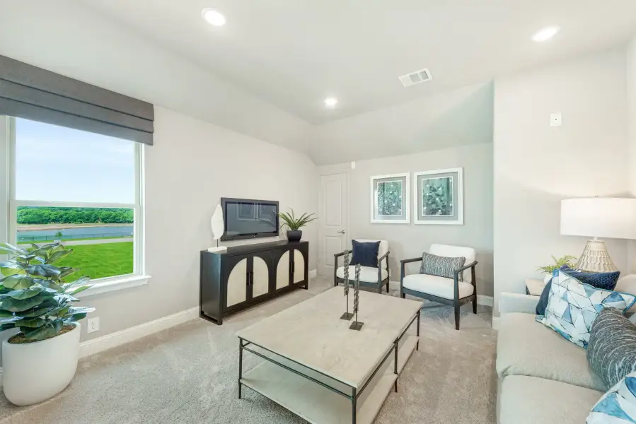 Carpeted living room with gray sofa, TV console, accent chair, and large window with water view