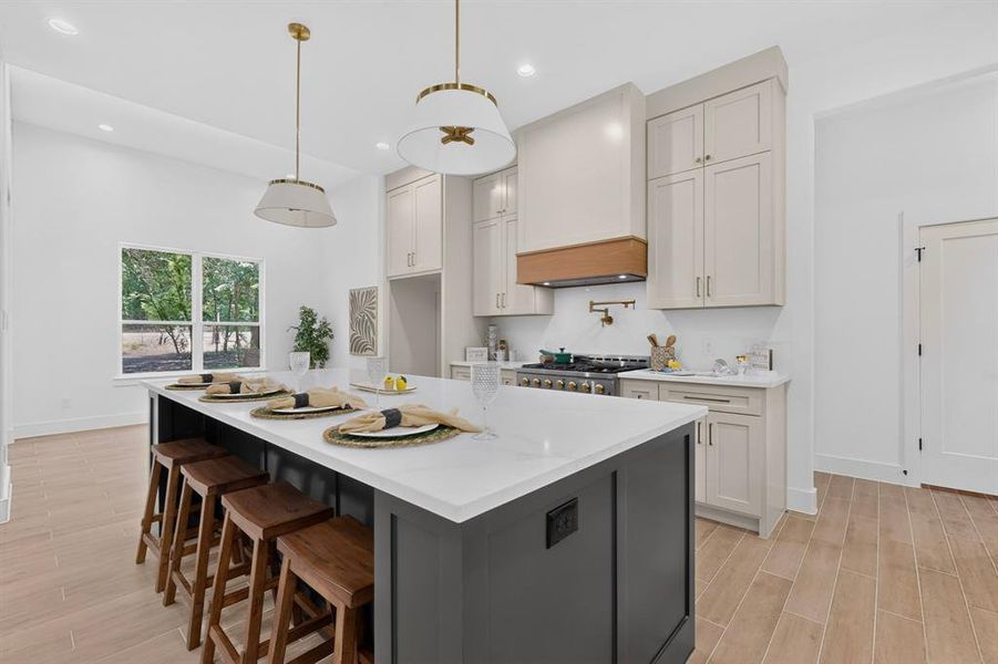 Kitchen featuring a large central island with seating, light-toned cabinetry, a built-in range hood with a wood accent, and wood-finish flooring