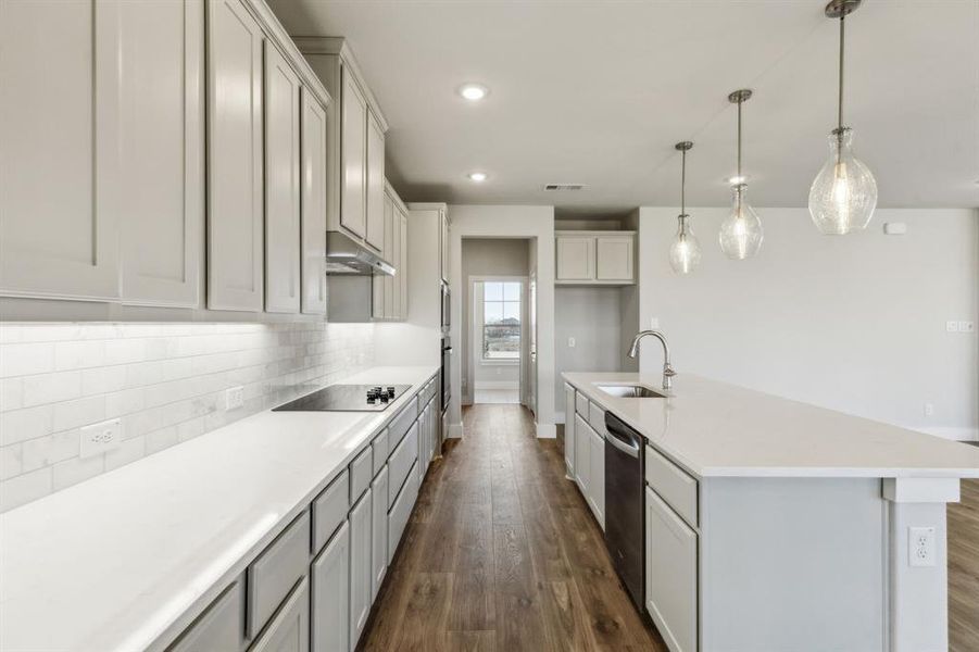 Kitchen with dishwasher, sink, hanging light fixtures, a kitchen island with sink, and black electric stovetop