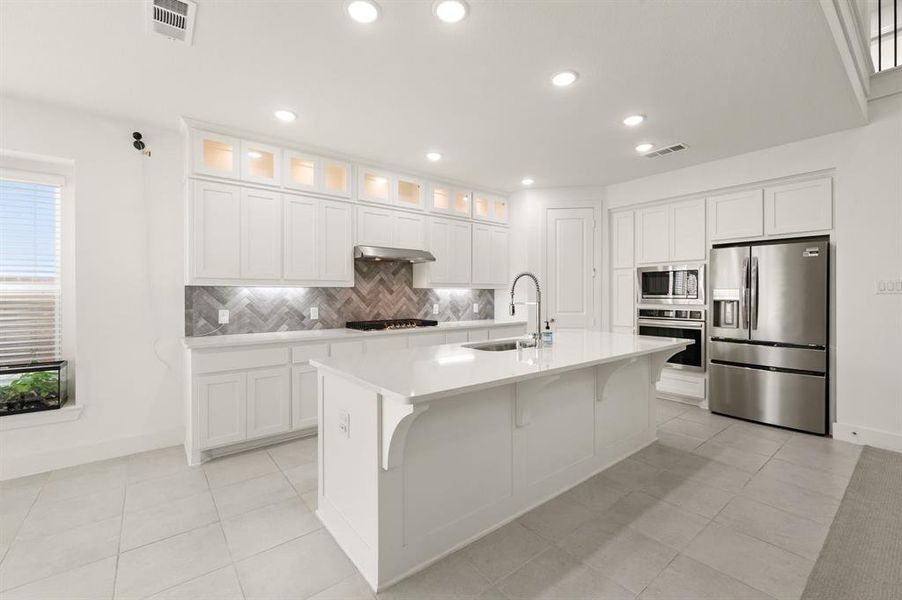 Kitchen with appliances with stainless steel finishes, white cabinetry, decorative backsplash, an island with sink, and a breakfast bar