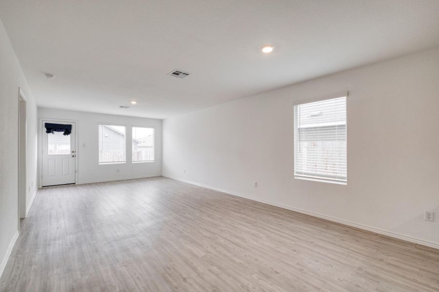Spacious room featuring wood-finish flooring, white walls, multiple windows with blinds, recessed lighting, and a rear exit door