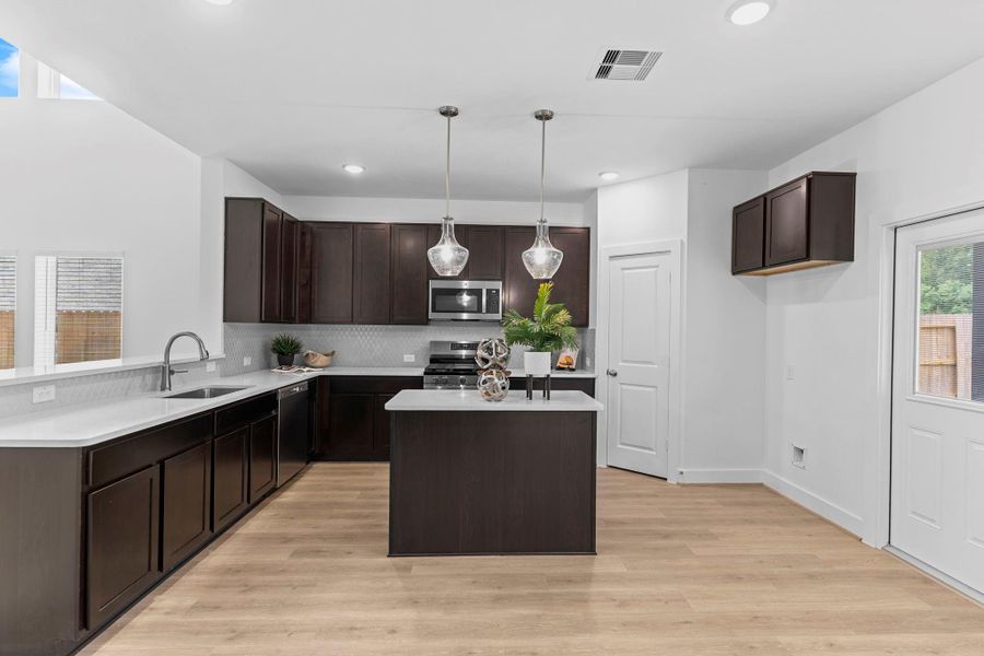 Striking kitchen design includes 42" upper cabinets, a gas range, built-in microwave, and walk-in pantry, all under recessed and pendant lighting that brings warmth and function. **Image Representative of Plan Only and May Vary as Built**.