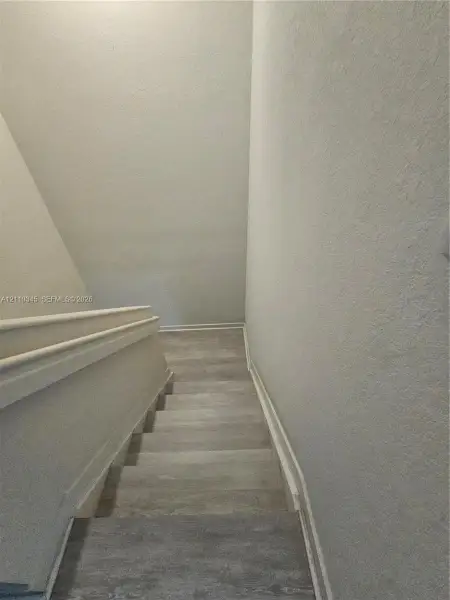 Staircase featuring wood-finish flooring and a painted wooden handrail