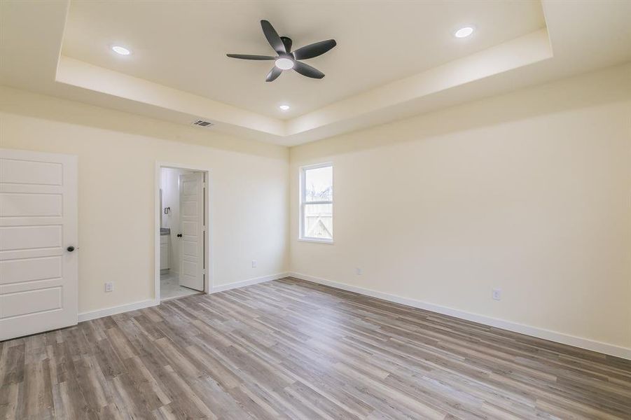 Unfurnished bedroom with ensuite bath, ceiling fan, hardwood / wood-style flooring, and a tray ceiling