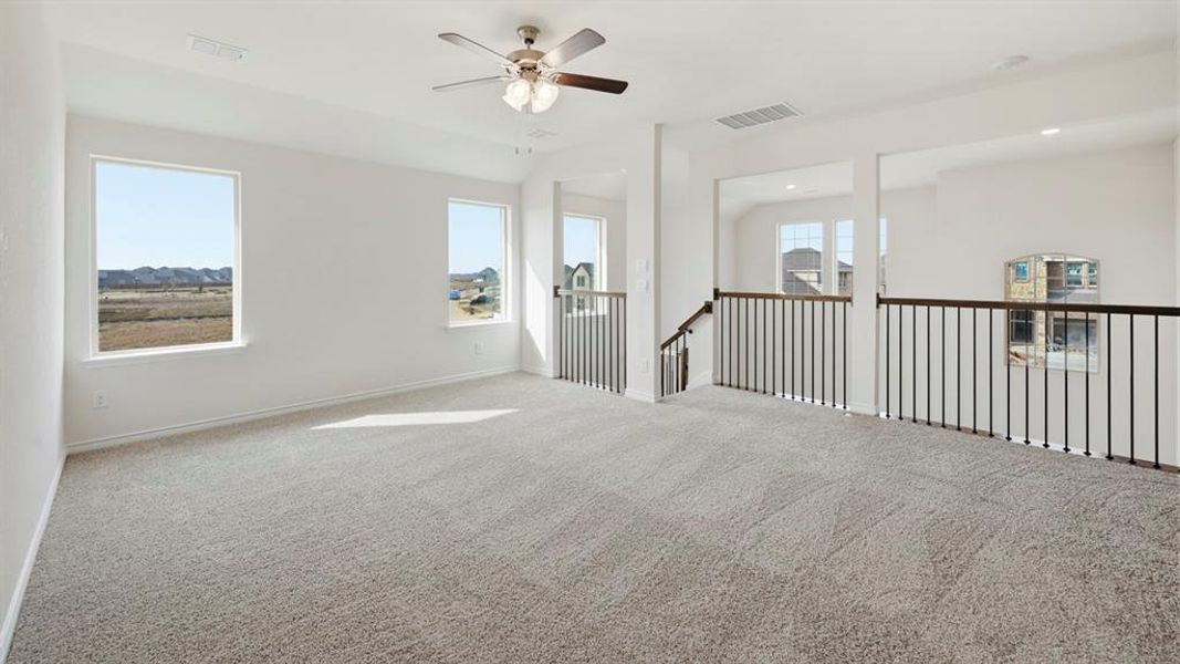 Spacious upper-level room featuring light gray carpeting, multiple windows providing natural light, a ceiling fan with integrated lighting, white painted walls, and an open railing overlooking the lower level Spacious upper-level room featuring light gray carpeting, multiple windows providing natural light, a ceiling fan with integrated lighting, white painted walls, and an open railing overlooking the lower level