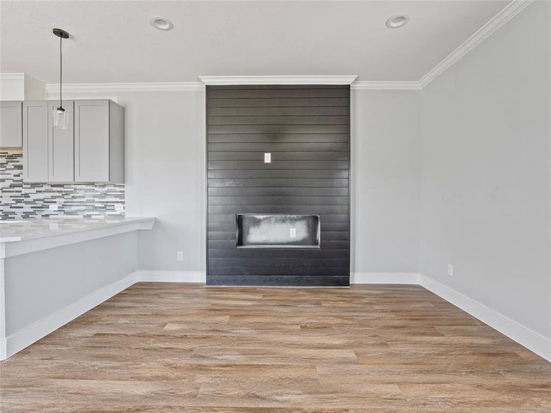Unfurnished living room featuring ornamental molding, light wood-style flooring, a large fireplace, baseboards, and recessed lighting