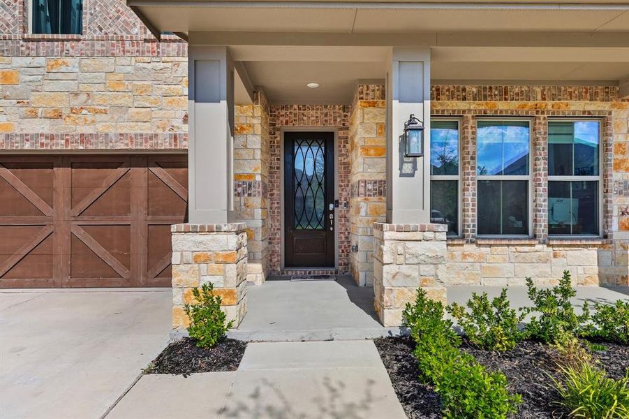 Doorway to property with a porch, stone siding, a garage, driveway, and brick siding Doorway to property with a porch, stone siding, a garage, driveway, and brick siding