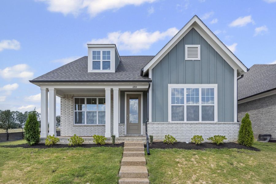 View of front facade with a front lawn, board and batten siding, brick siding, a porch, and roof with shingles