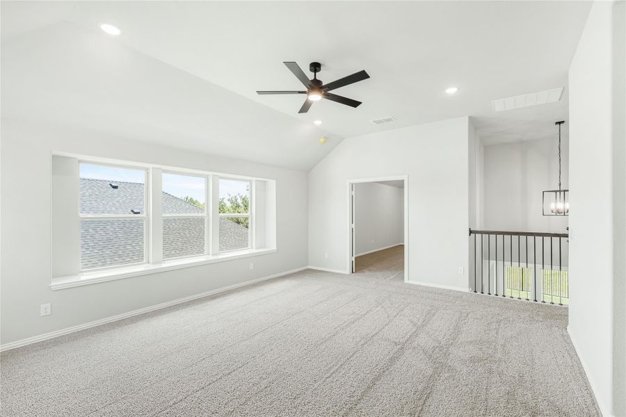 Spacious upstairs bedroom with vaulted ceiling, ceiling fan, carpet flooring, and large windows overlooking neighboring rooftops. Spacious upstairs bedroom with vaulted ceiling, ceiling fan, carpet flooring, and large windows overlooking neighboring rooftops.
