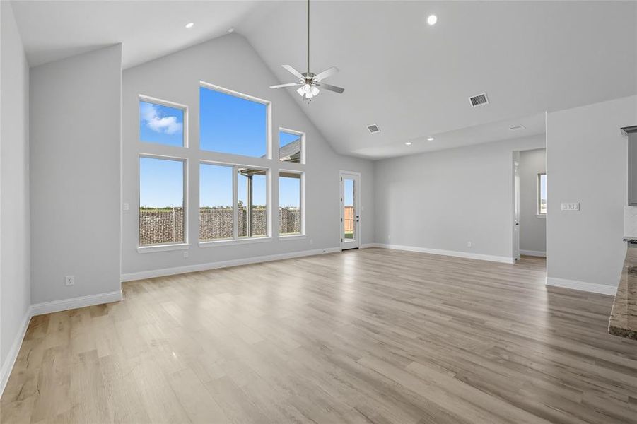 Unfurnished living room featuring high vaulted ceiling, plenty of natural light, light wood-style floors, recessed lighting, and a ceiling fan Unfurnished living room featuring high vaulted ceiling, plenty of natural light, light wood-style floors, recessed lighting, and a ceiling fan
