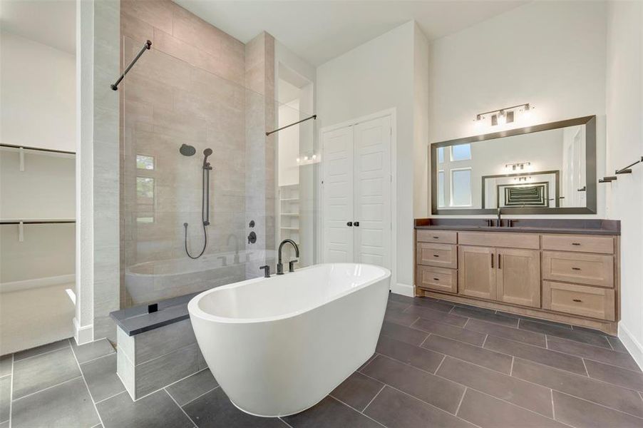 Full bath with a walk in shower, a soaking tub, vanity, a walk in closet, and dark tile patterned flooring