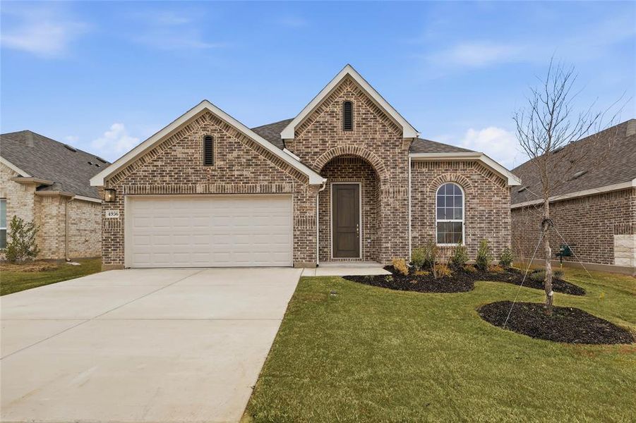 View of front facade with brick siding, an attached garage, concrete driveway, a front lawn, and roof with shingles