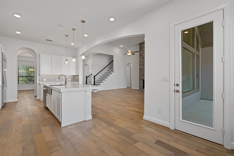 Open-concept kitchen featuring an island with a stainless steel sink, white cabinetry, and pendant lighting