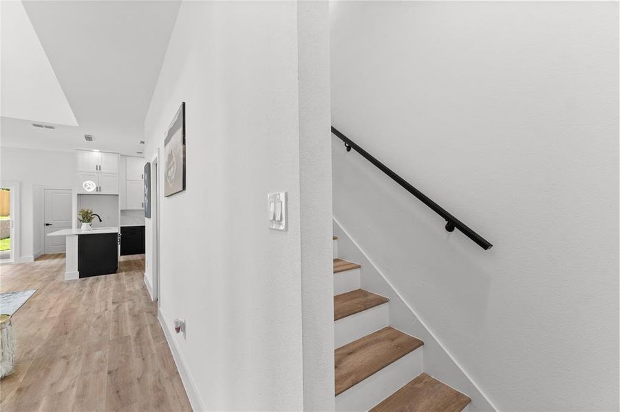 Contemporary interior featuring light wood-finish flooring and a minimalist staircase with a black handrail