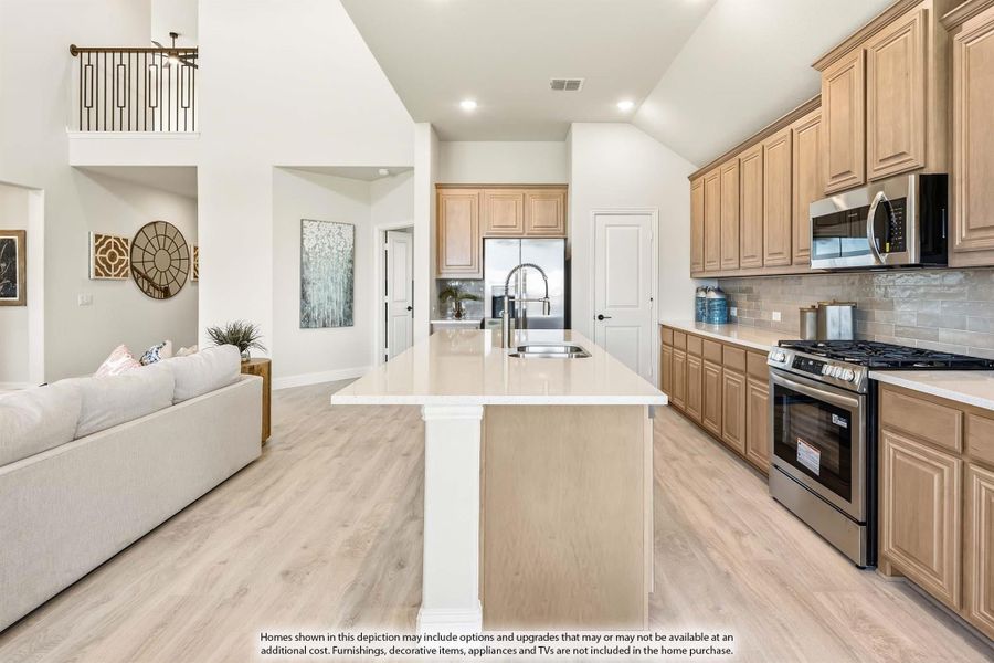 Open kitchen with tan cabinets, center island, stainless appliances, and light wood floors, open to living area with high ceilings