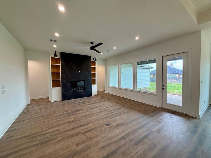 Unfurnished living room featuring a ceiling fan, dark wood-style flooring, recessed lighting, a tile fireplace, and built in features