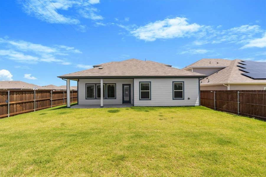 Expansive fenced backyard featuring a covered patio with concrete flooring, white siding, and a dark brown shingled roof