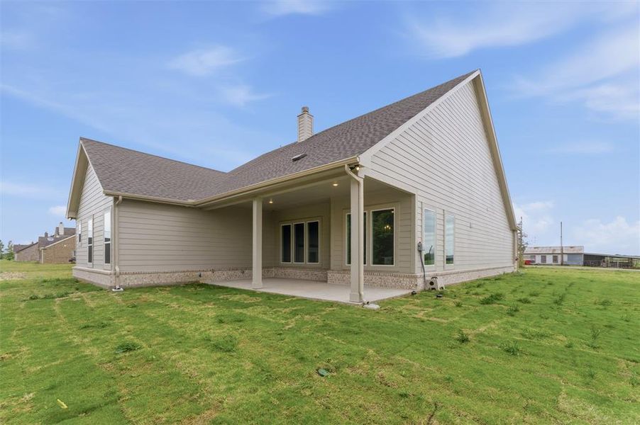 Rear view of property with roof with shingles, a patio area, a lawn, and a chimney