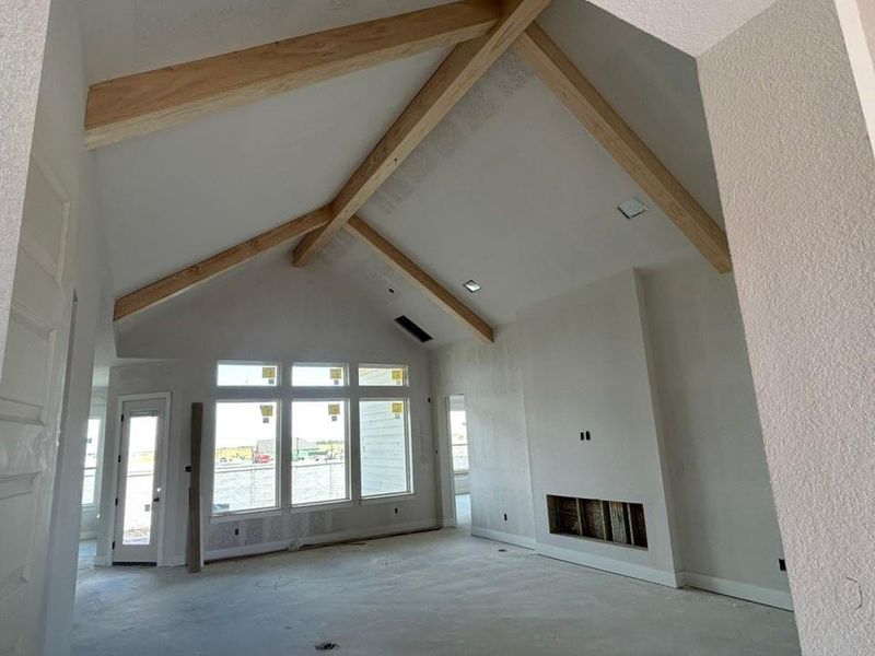 Unfurnished living room with high vaulted ceiling, beamed ceiling, a fireplace, and unfinished concrete floors Unfurnished living room with high vaulted ceiling, beamed ceiling, a fireplace, and unfinished concrete floors