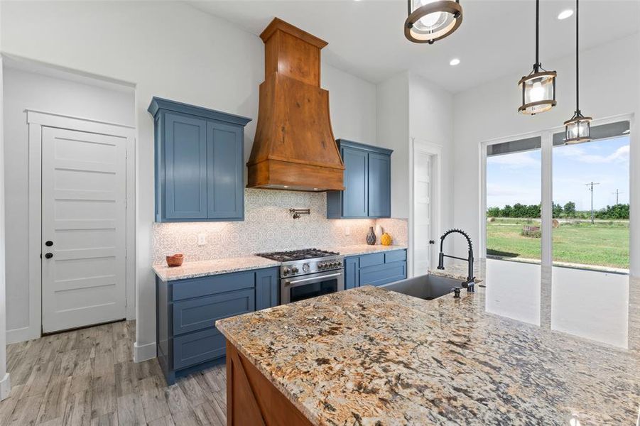 Kitchen featuring a large central island with granite countertop, blue cabinetry, a wood-finish range hood, stainless steel gas range, and large windows