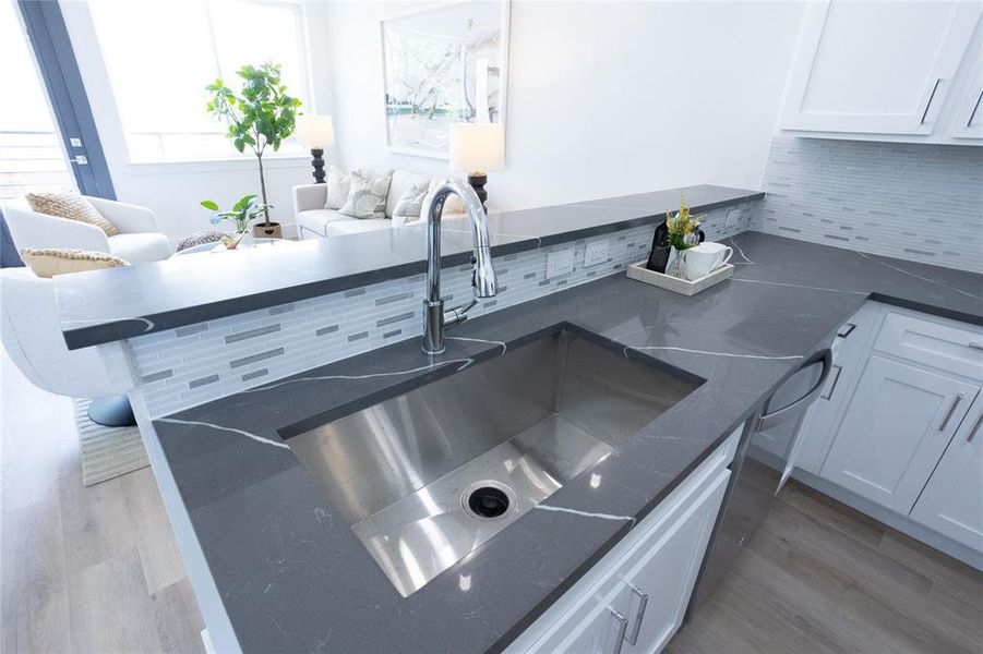 Kitchen featuring hardwood / wood-style flooring, white cabinetry, tasteful backsplash, and sink