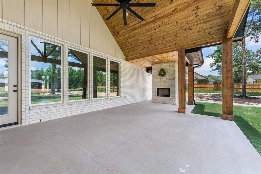 Covered outdoor patio featuring a stone-clad fireplace and wood-finish ceiling with a ceiling fan