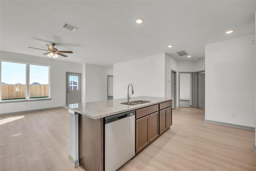 Kitchen with dishwasher, open floor plan, light stone counters, a ceiling fan, and a kitchen island with sink