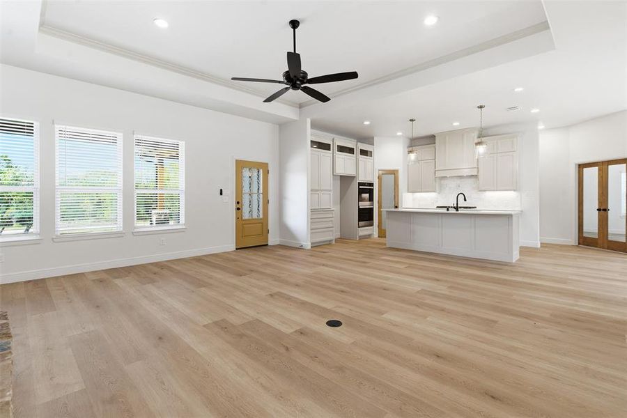 Unfurnished living room featuring a raised ceiling, light wood-style flooring, recessed lighting, a ceiling fan, and ornamental molding Unfurnished living room featuring a raised ceiling, light wood-style flooring, recessed lighting, a ceiling fan, and ornamental molding