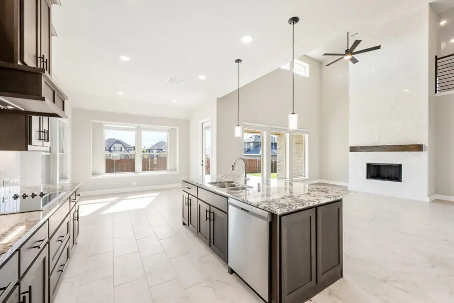 Open kitchen with large island, granite countertops, dark cabinets, and vaulted ceiling open to living area with fireplace.