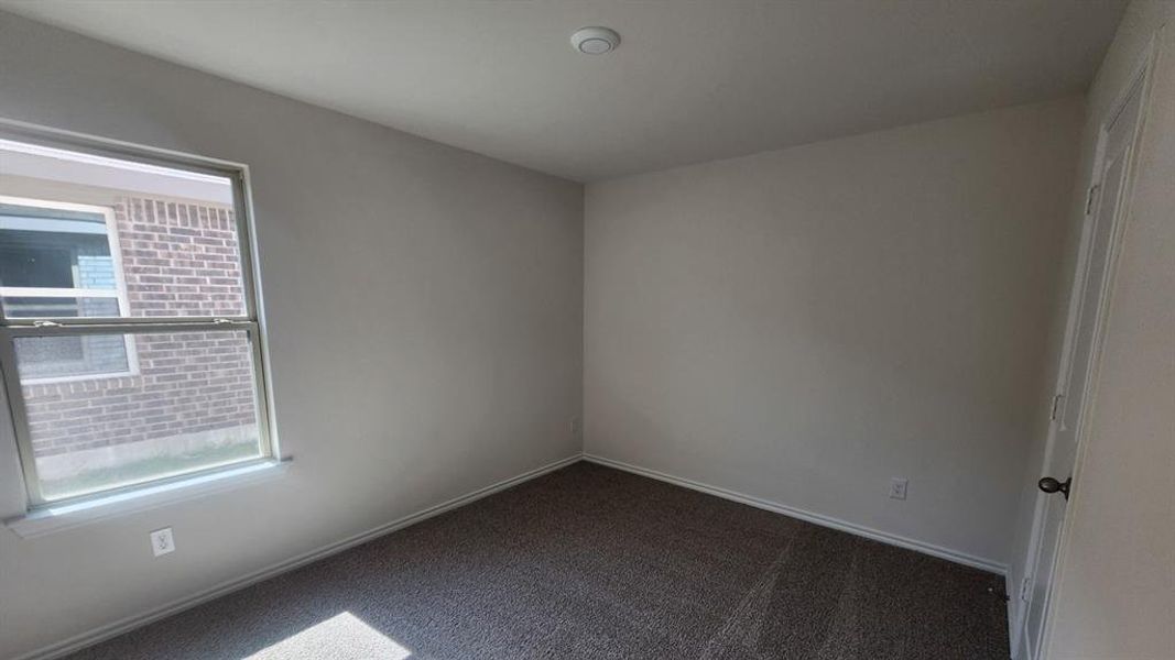 Bright room featuring neutral-toned walls, textured carpet flooring, and a double-hung window with exterior brick exposure