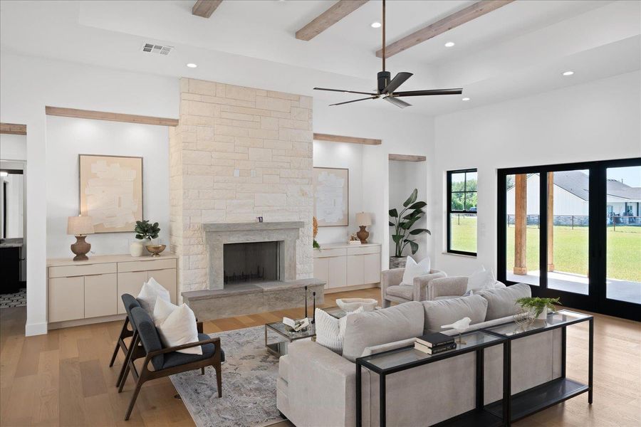 Living room with beamed ceiling, light wood-type flooring, ceiling fan, a towering ceiling, and a fireplace