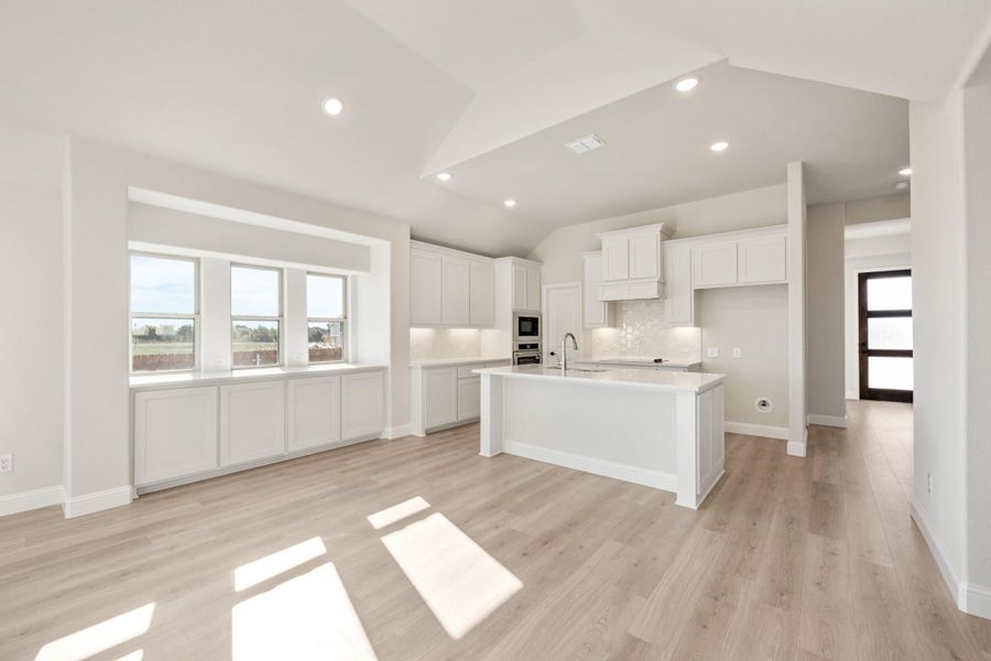Open kitchen with white cabinets, center island, and light wood floors in a bright open layout