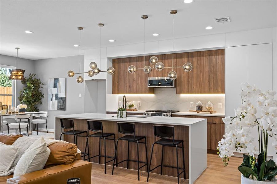 Kitchen with modern cabinets, brown cabinets, a breakfast bar, a center island with sink, and recessed lighting Kitchen with modern cabinets, brown cabinets, a breakfast bar, a center island with sink, and recessed lighting