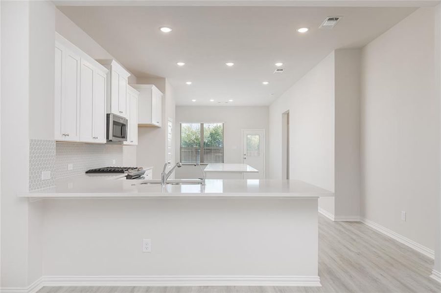 Kitchen featuring kitchen peninsula, decorative backsplash, white cabinetry, light wood-type flooring, and sink