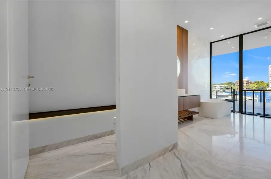 Stone-tiled flooring, wall-mounted wood-finish vanity, freestanding soaking tub, recessed ceiling lighting, and floor-to-ceiling glass sliding doors
