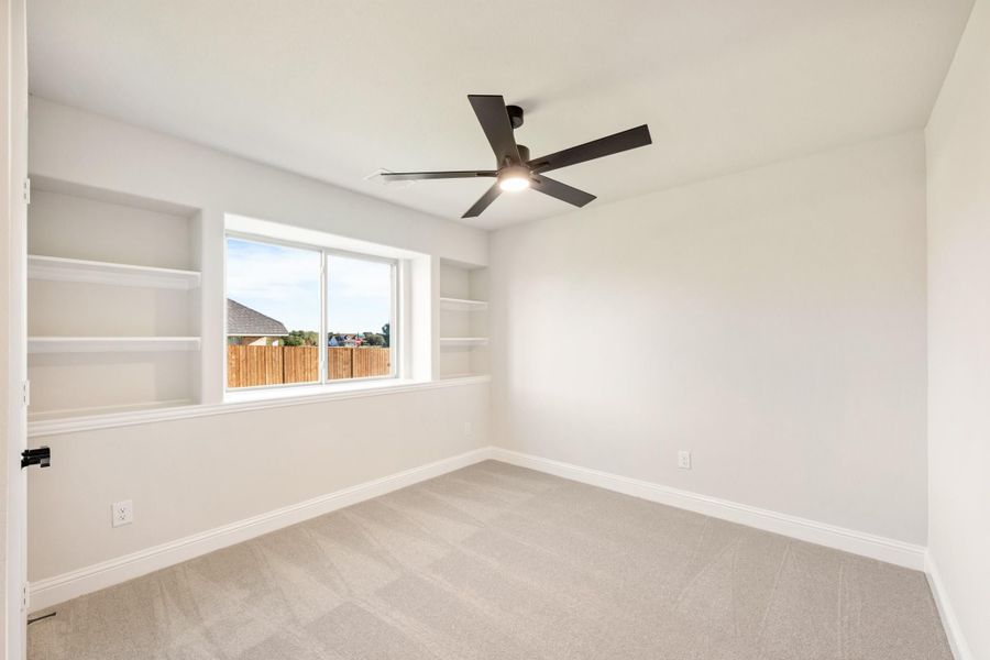 Empty bedroom with built-in shelves, ceiling fan, carpet flooring, and a large window with backyard view