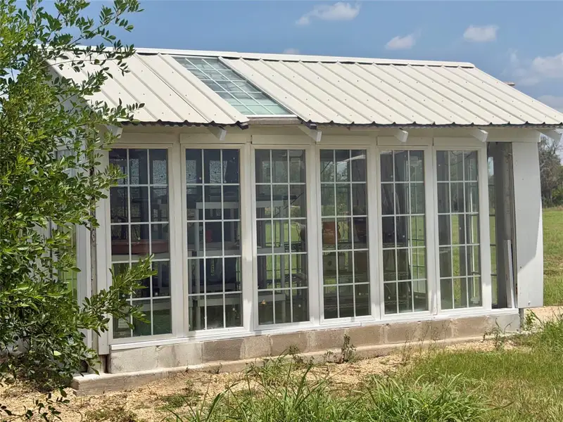 A quaint greenhouse with a metal roof and numerous multi-pane windows offers abundant light for cultivation.