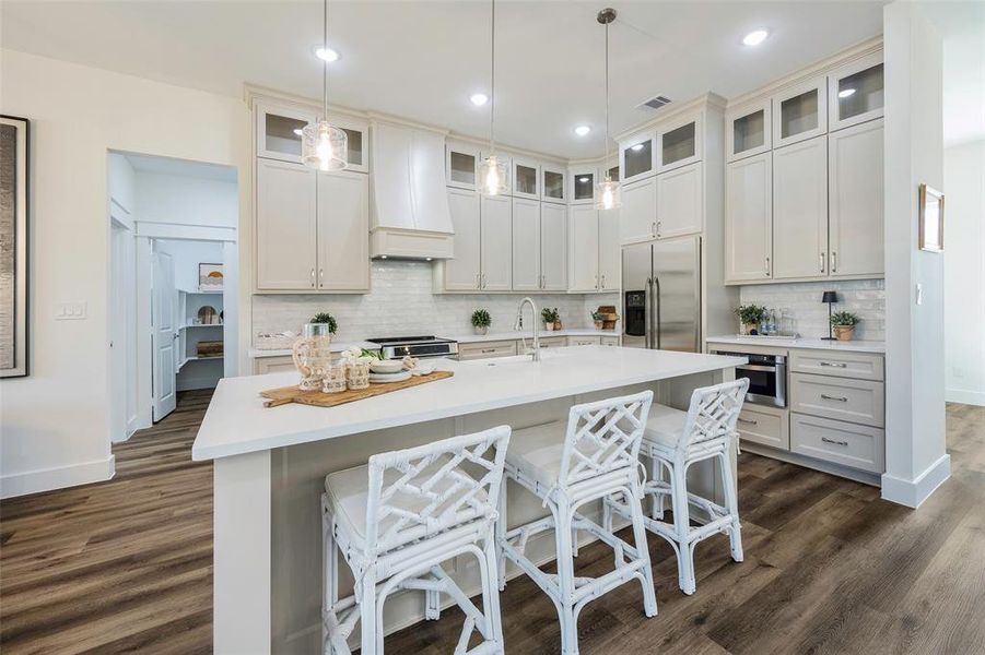 Gourmet kitchen featuring expansive island with farmhouse sink and breakfast bar seating. Abundant storage throughout with stunning greige floor-to-ceiling cabinetry and decorative glass uppers. Complete with electric range and hood, dishwasher, and convenient microwave drawer.