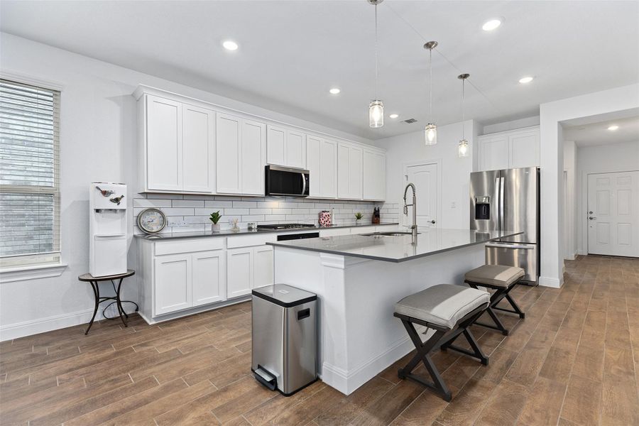 Kitchen with a kitchen bar, stainless steel appliances, white cabinetry, pendant lighting, and an island with sink