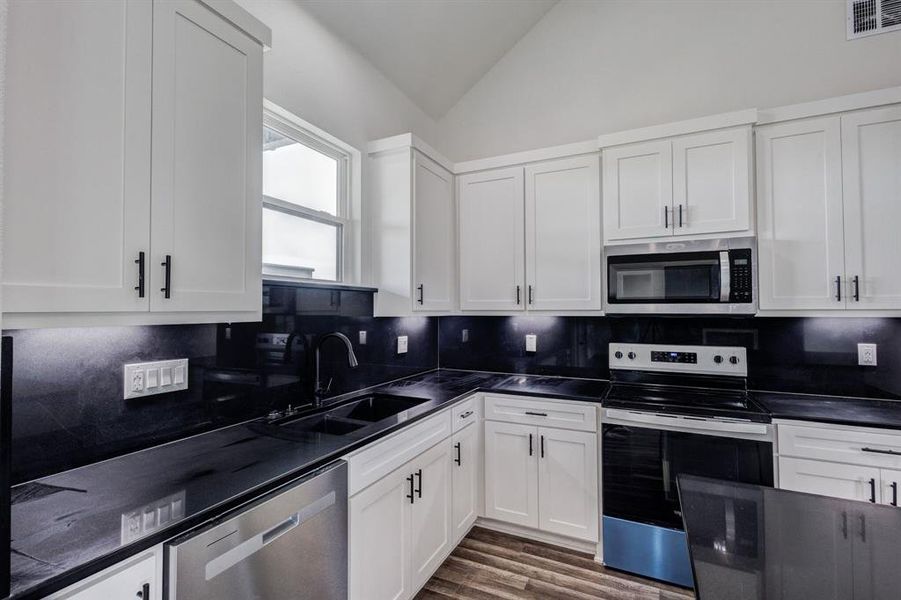 The kitchen features white cabinetry with dark hardware, black countertops, and a black backsplash