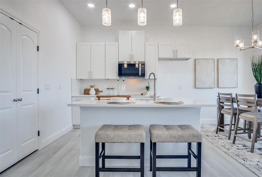 Kitchen featuring white cabinetry, a breakfast bar, light wood-style floors, hanging light fixtures, and stainless steel microwave Kitchen featuring white cabinetry, a breakfast bar, light wood-style floors, hanging light fixtures, and stainless steel microwave